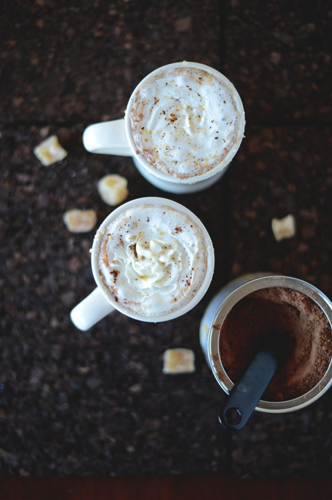 Two mugs of dairy-free Ginger Hot Chocolate and a container of cocoa powder