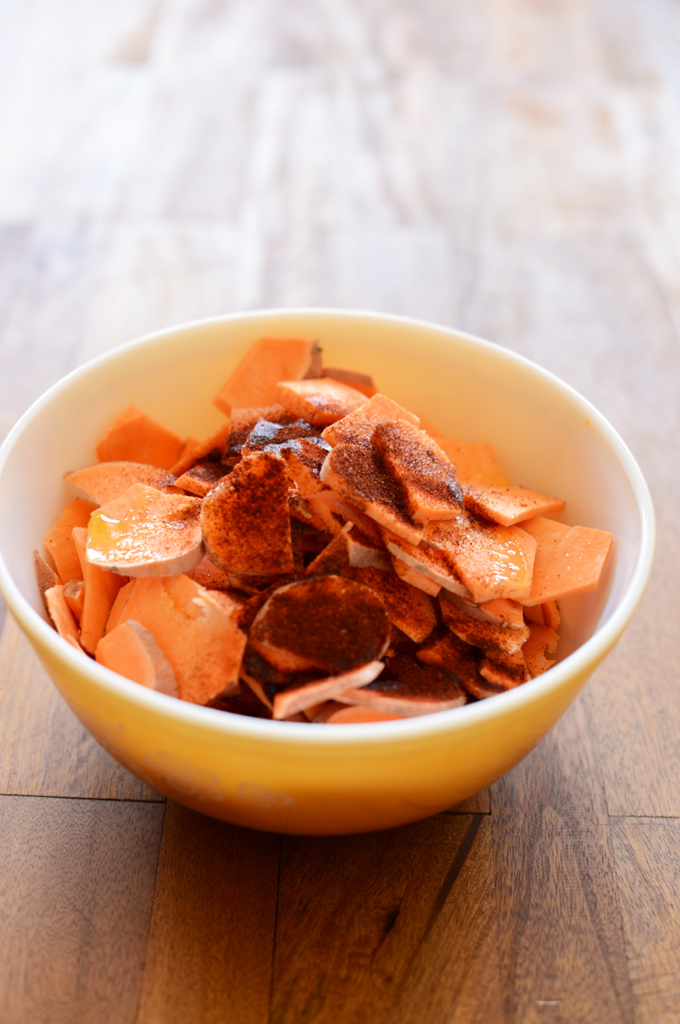 Bowl of sweet potato slices topped with oil and spices for making Chipotle Spiced Sweet Potatoes
