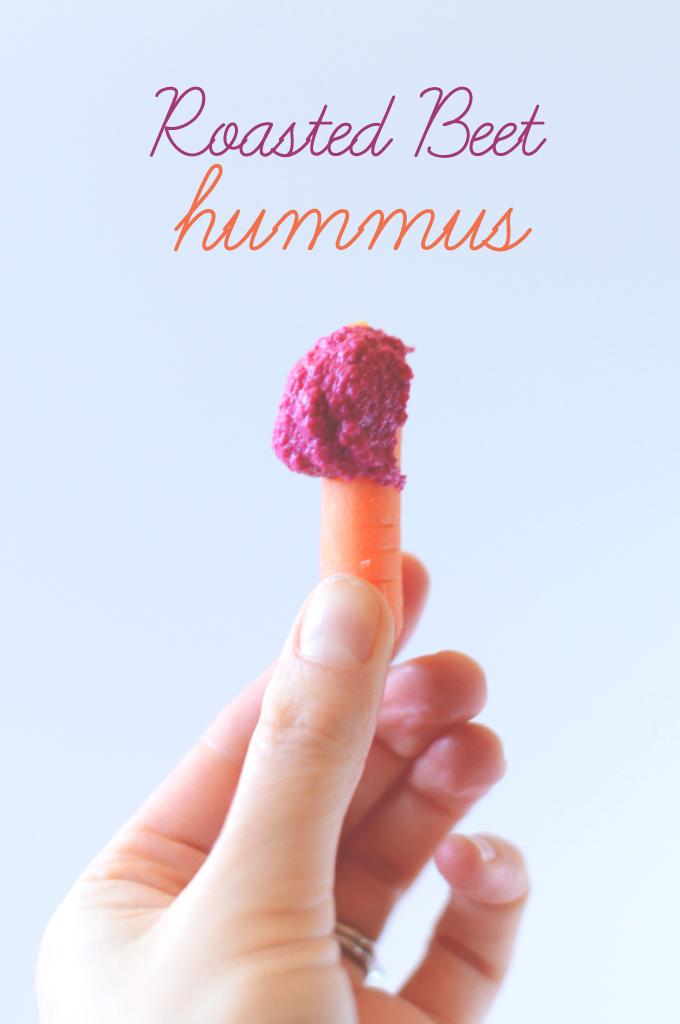 Holding up a baby carrot dipped in Roasted Beet Hummus