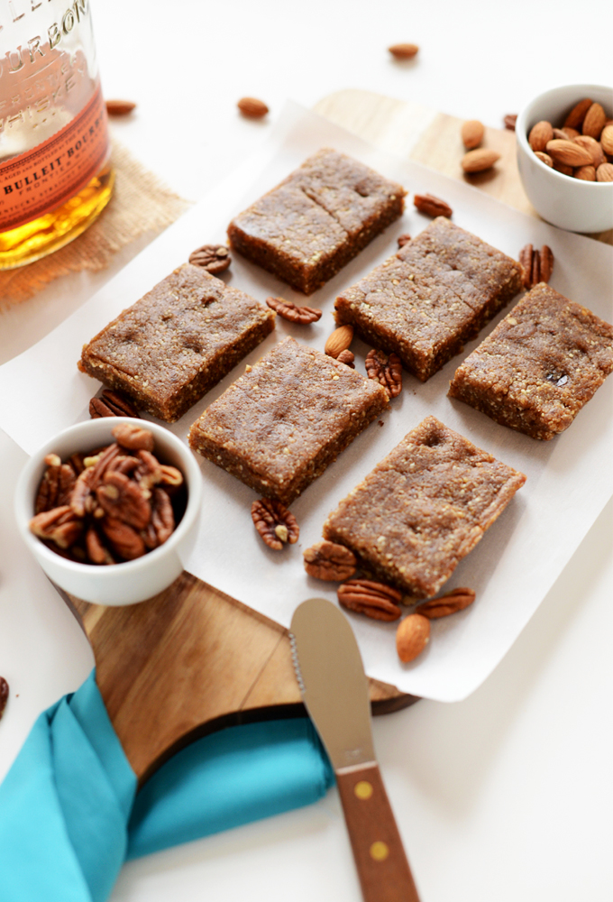 Batch of cut Boozy Pecan Pie Bars on a cutting board surrounded by almonds and pecans
