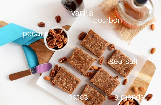 Parchment-lined cutting board of Raw Boozy Pecan Pie Bars surrounded by ingredients used to make them
