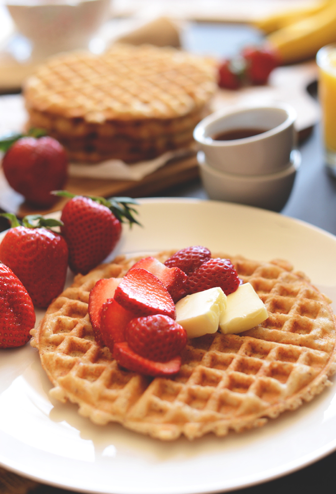 Plate with a homemade gluten-free waffle topped with vegan butter and strawberries