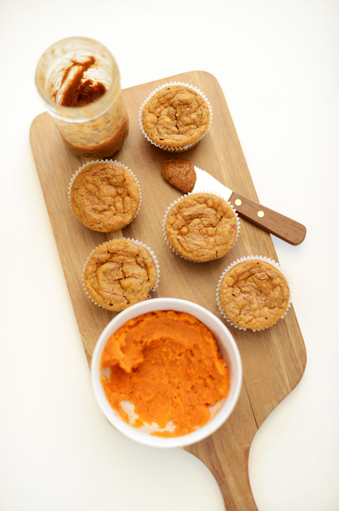 Cutting board with a batch of Vegan Sweet Potato Almond Butter Muffins alongside ingredients used to make them