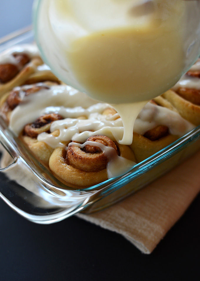 Drizzling icing over a batch of Vegan Cinnamon Rolls
