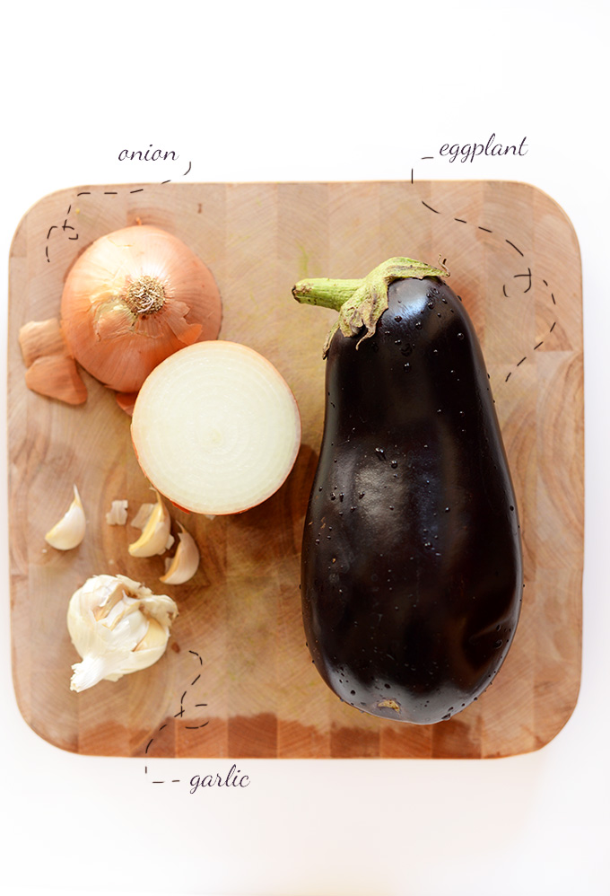 Cutting board with onions, garlic, and eggplant for making Persian Eggplant Dip