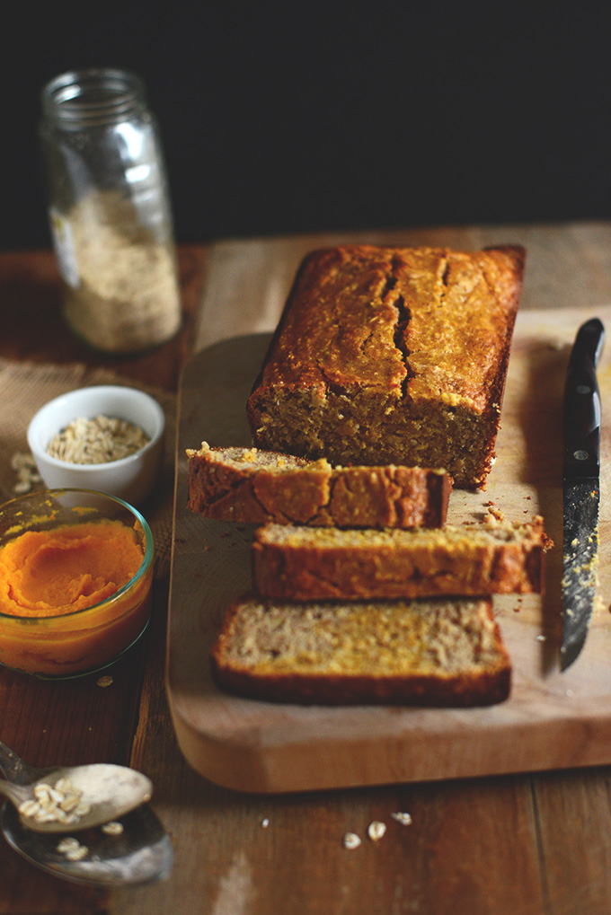 Cascading partially sliced loaf of Gluten-Free Banana Bread with bowls of oats and squash