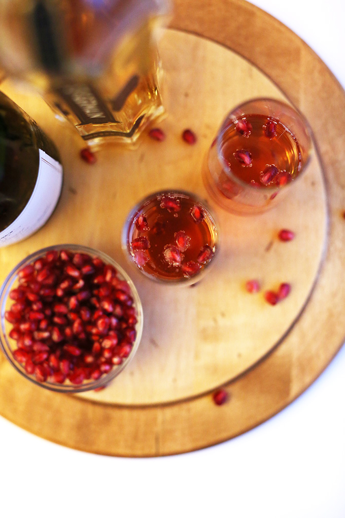 Tall glasses of Pomegranate St. Germain Spritzers surrounded by ingredients used to make them