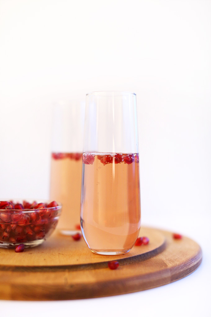 Bowl of pomegranate seeds and two tall glasses filled with our Pomegranate Spritzers recipe