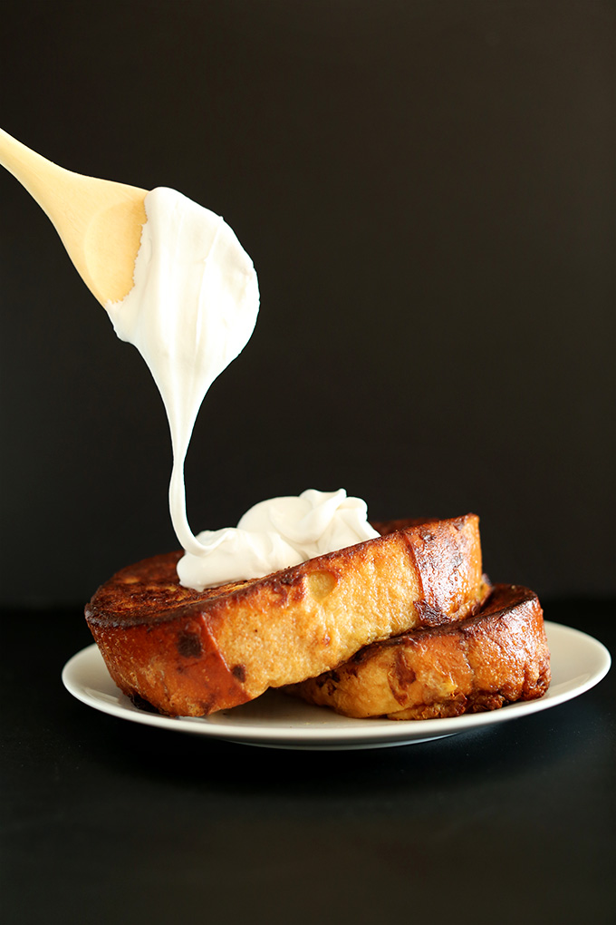 Drizzling coconut whipped cream onto two slices of Coconut Cream Pie French Toast