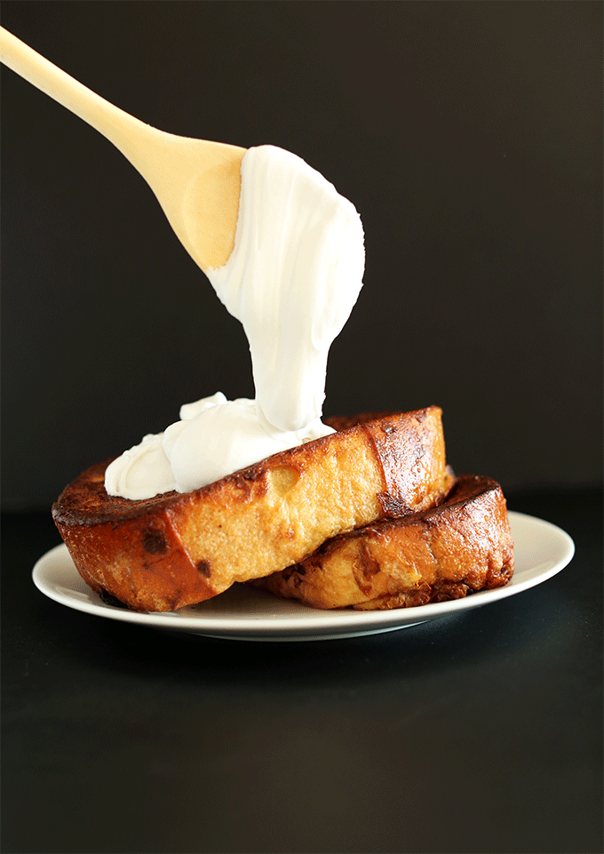 Using a wooden spoon to drizzle coconut whipped cream onto Coconut French Toast
