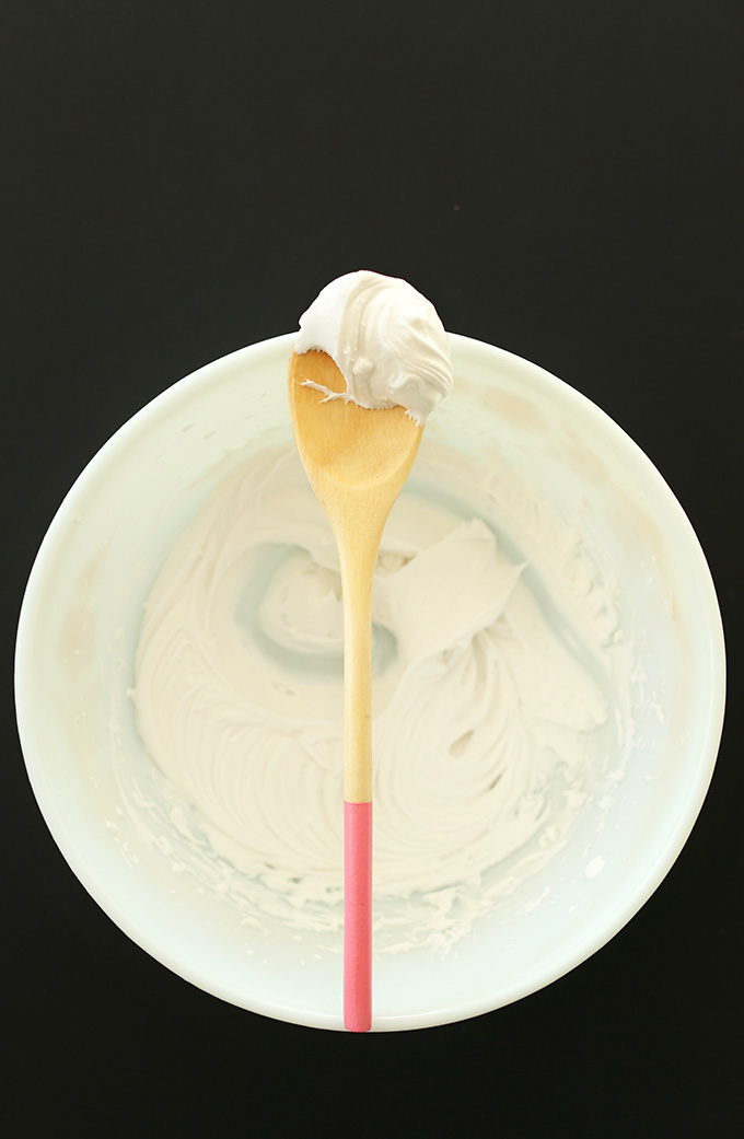 Holding up a wooden spoon of coconut whipped cream over a bowl