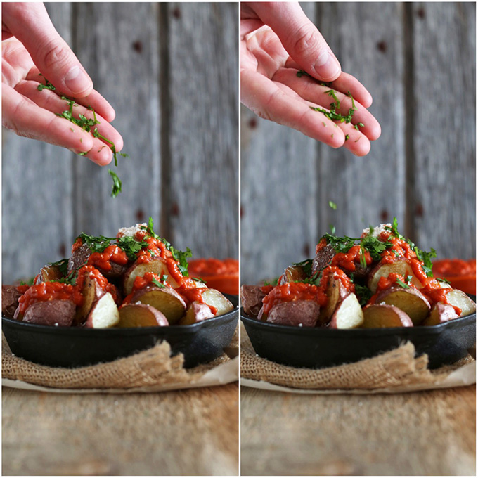 Sprinkling fresh parsley onto a cast-iron skillet filled with Patatas Bravas with Spicy Tomato Sauce