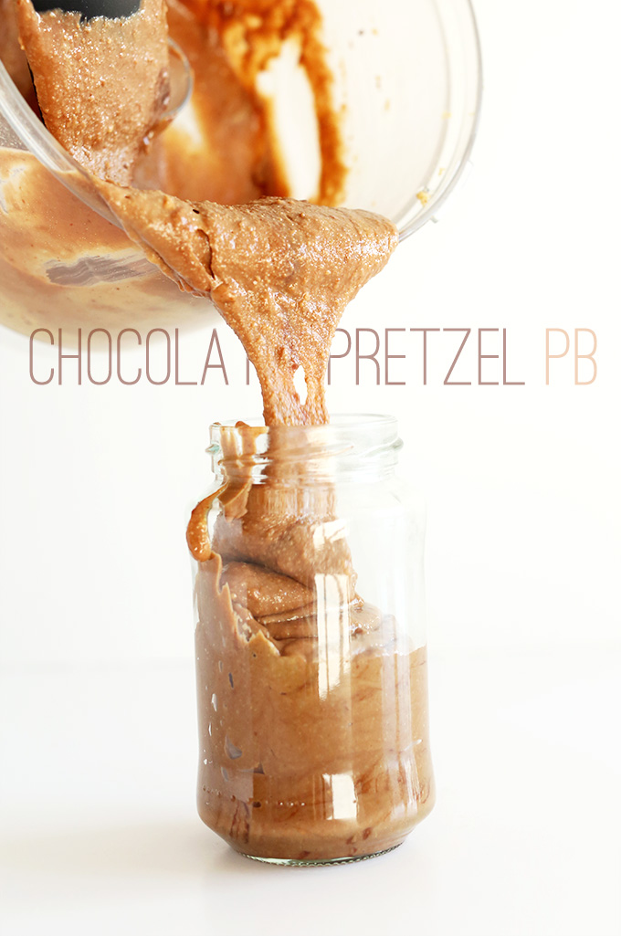 Using a rubber spatula to scoop homemade Chocolate Pretzel Peanut Butter into a jar