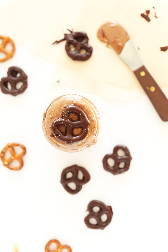 Chocolate covered pretzels surrounding and resting on a jar of Chocolate Pretzel Peanut Butter