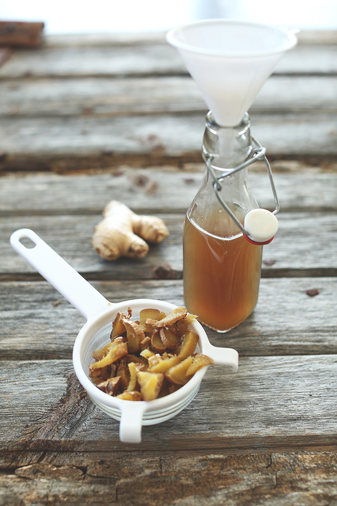 Jar of ginger syrup with a funnel resting on it and pieces of strained ginger