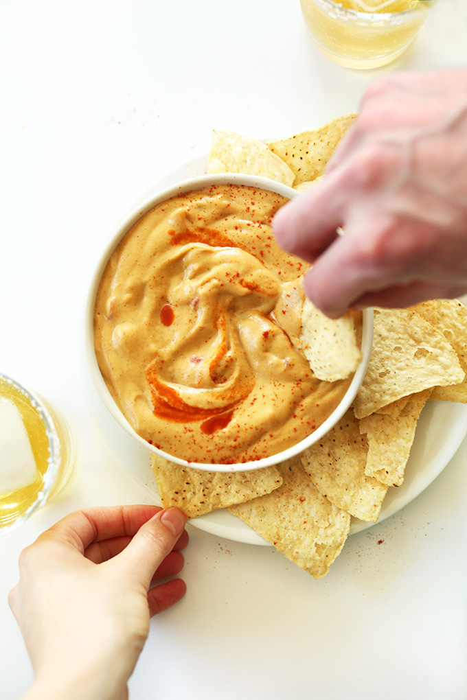 Dipping chips into Creamy Vegan Queso with a hot sauce swirl