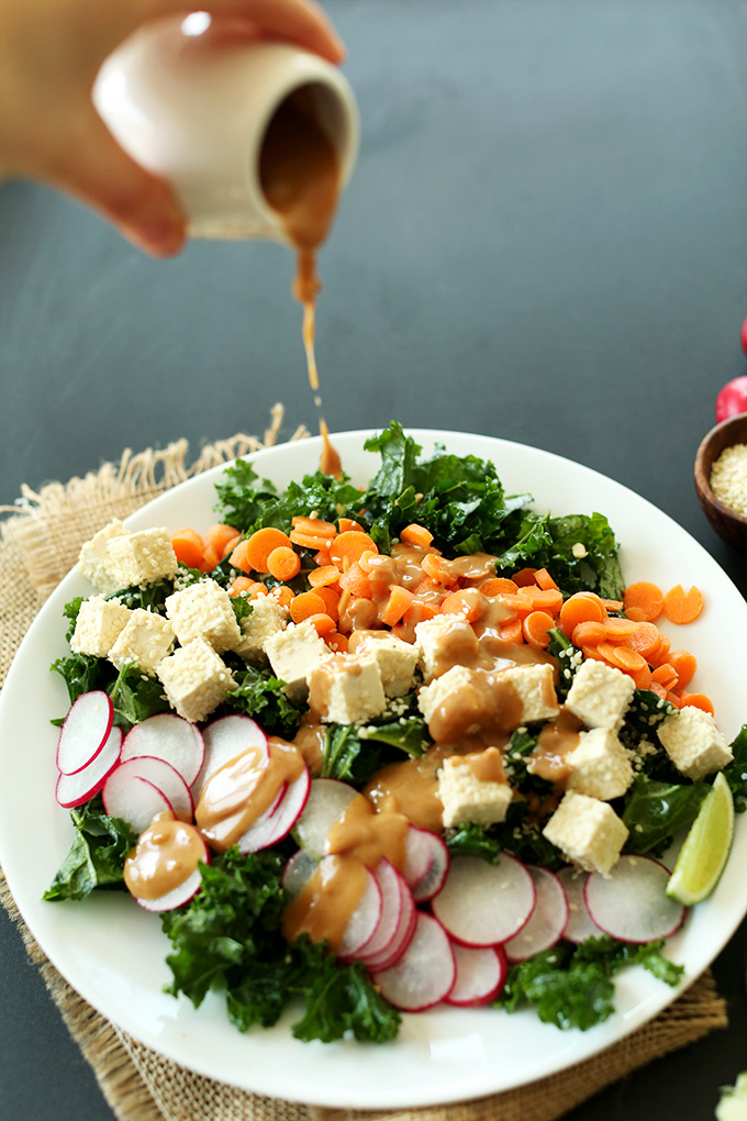 Pouring peanut dressing over Thai Kale Salad for a simple vegan gluten-free dinner