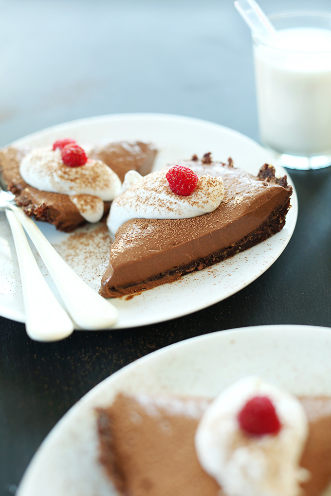 Slices of Vegan Chocolate Silk Pie topped with coconut whipped cream and fresh raspberries