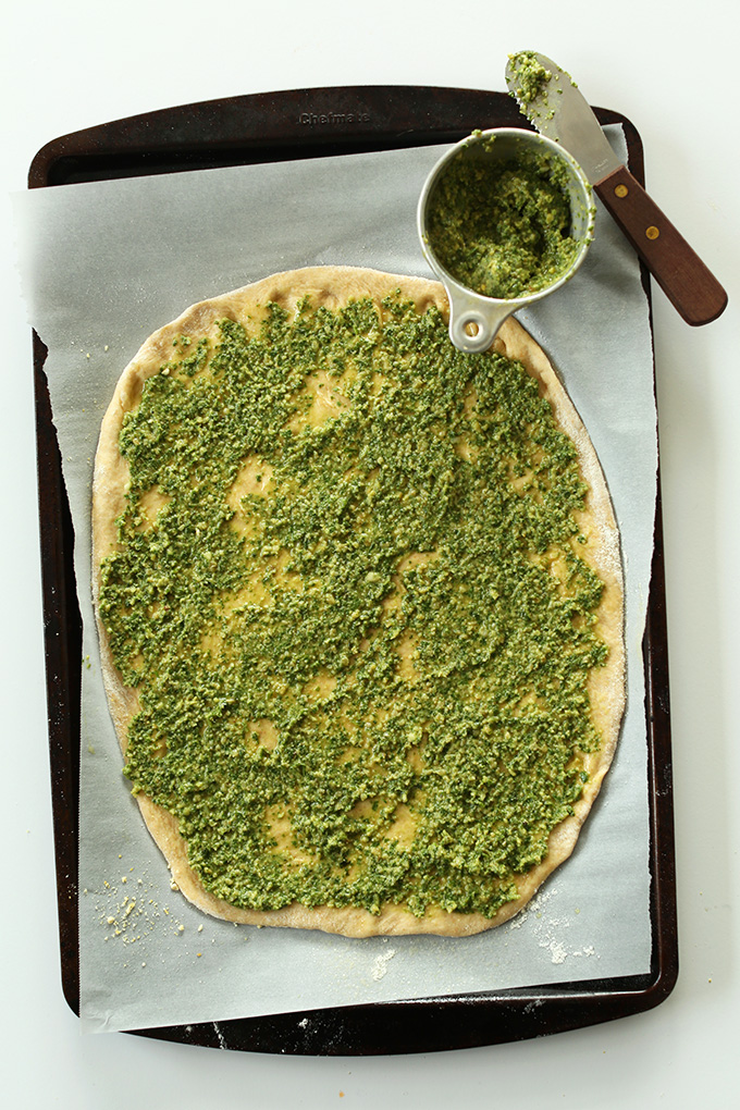 Parchment-lined baking sheet with vegan breadstick dough slathered with pesto