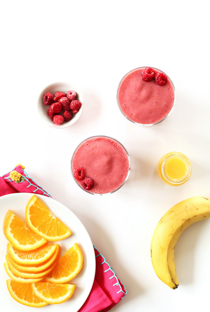Two glasses of our Summer in a Cup Smoothie recipe surrounded by ingredients used to make it