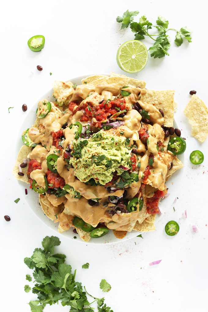 Plate of gluten-free vegan nachos piled high with queso, salsa, and guacamole
