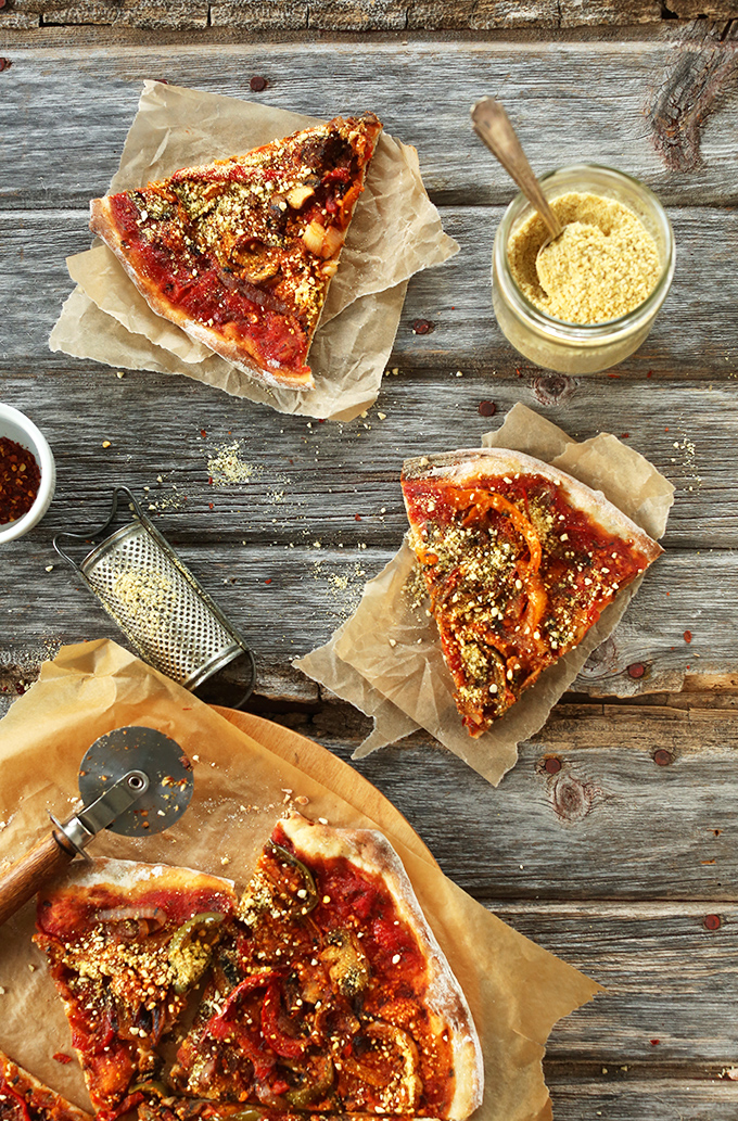 Slices of The Best Vegan Pizza alongside dishes of vegan parmesan cheese and red chili flakes