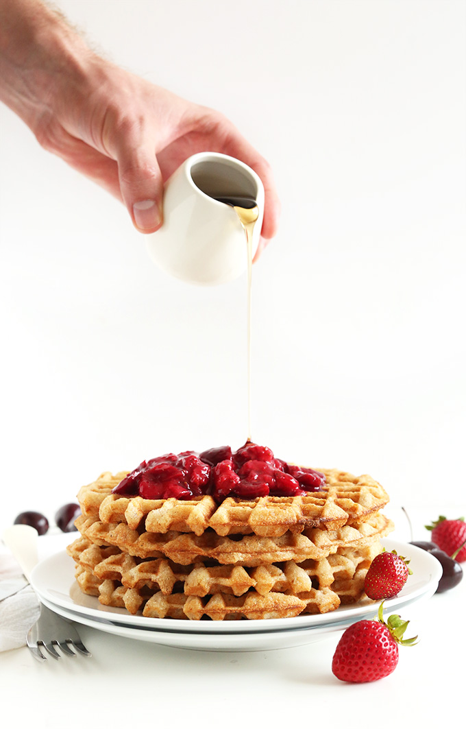 Drizzling maple syrup onto Vegan Gluten-Free Waffles topped with fruit compote
