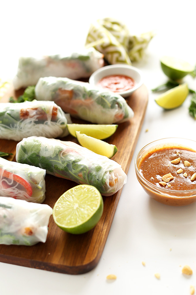 Batch of our homemade Vegan Spring Rolls on a cutting board with fresh limes and dipping sauce