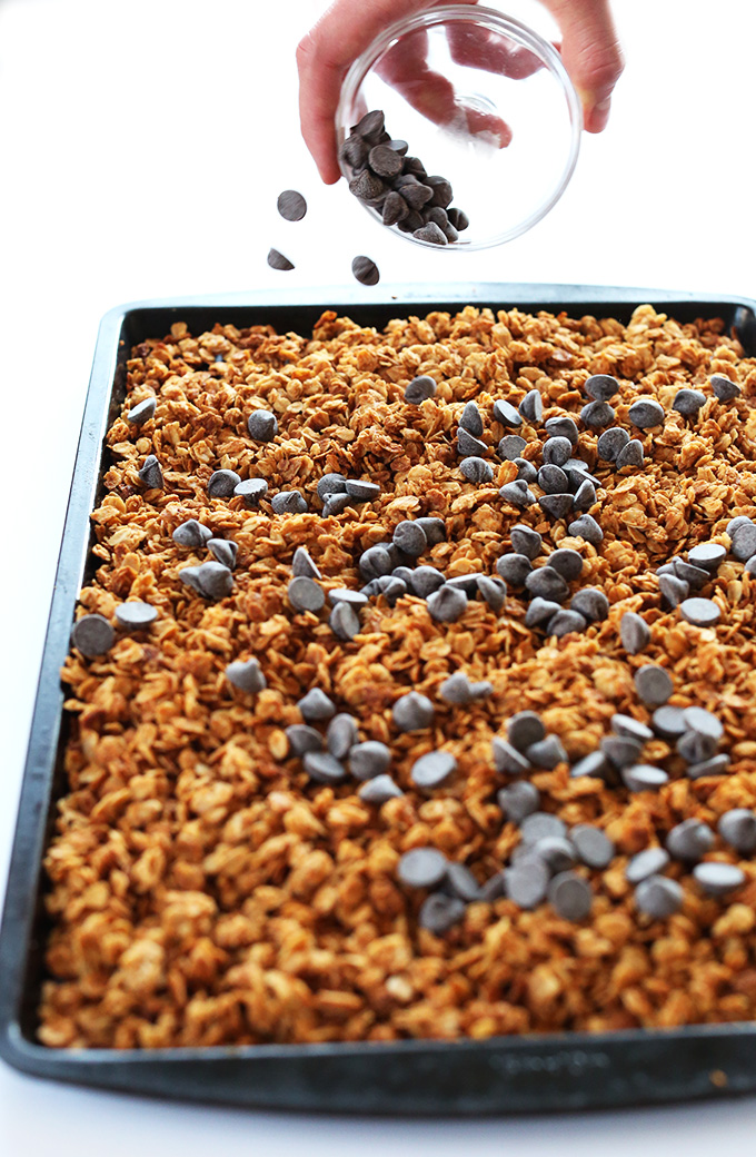 Sprinkling chocolate chips onto a baking sheet filled with Gluten-Free Peanut Butter Granola