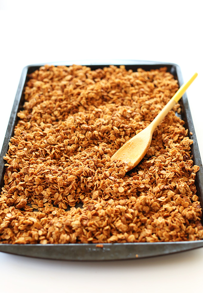Wooden spoon resting on a baking sheet filled with Peanut Butter Chocolate Chip Granola