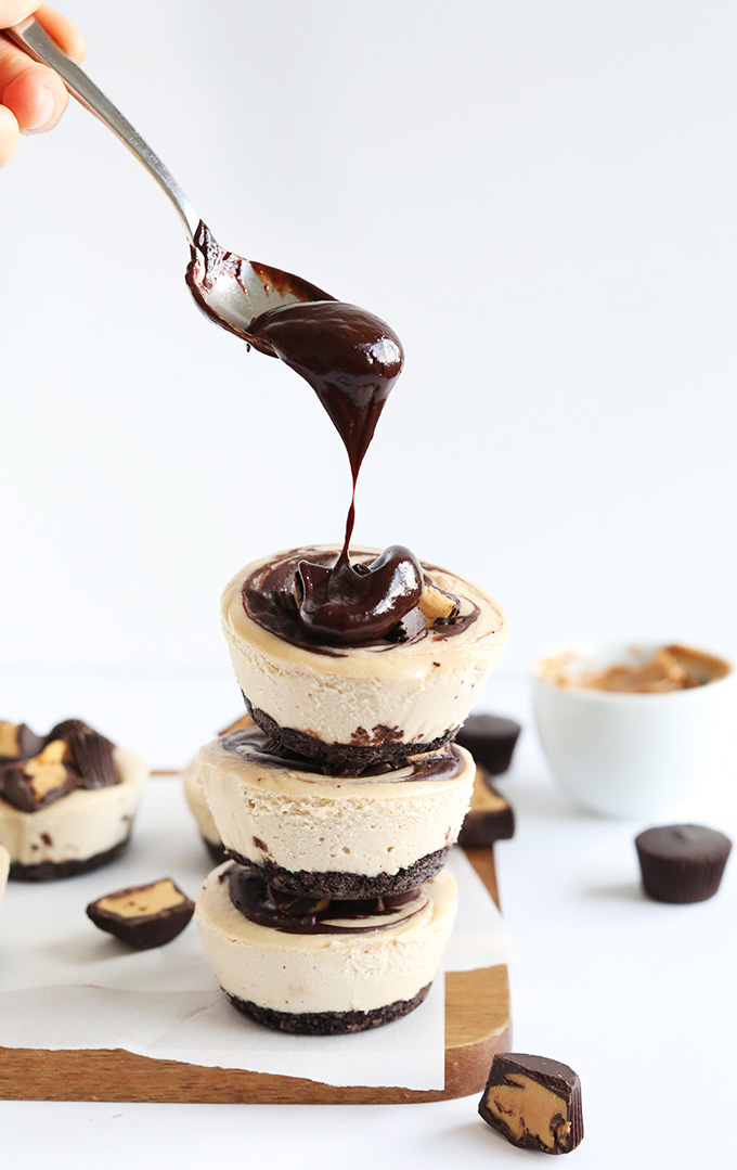 Adding a chocolate fudge drizzle onto a stack of homemade Vegan Peanut Butter Cup Cheesecakes