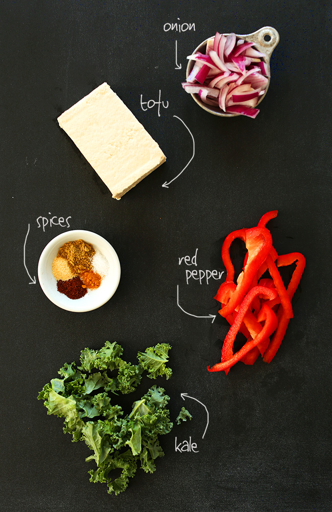 Tofu, onion, red pepper, kale, and spices on a dark background