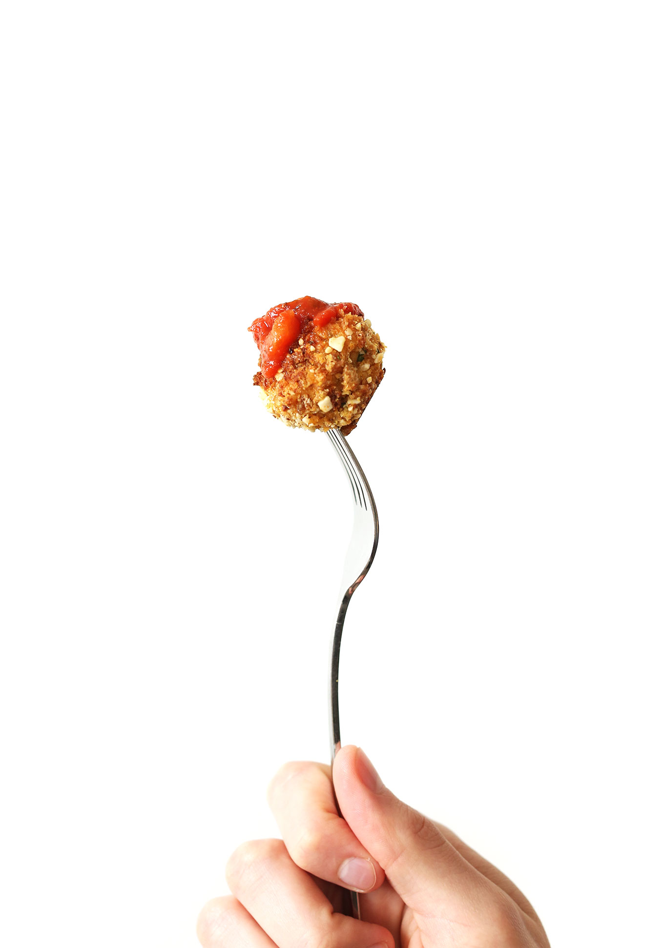 Holding up a marinara-dipped vegan meatball on a fork