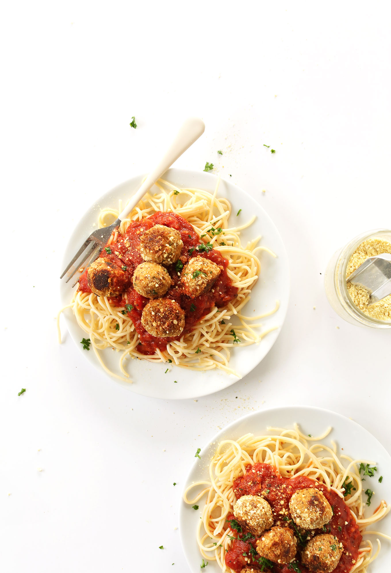 Plates of pasta topped with marinara, vegan meatballs, parsley, and vegan parmesan cheese