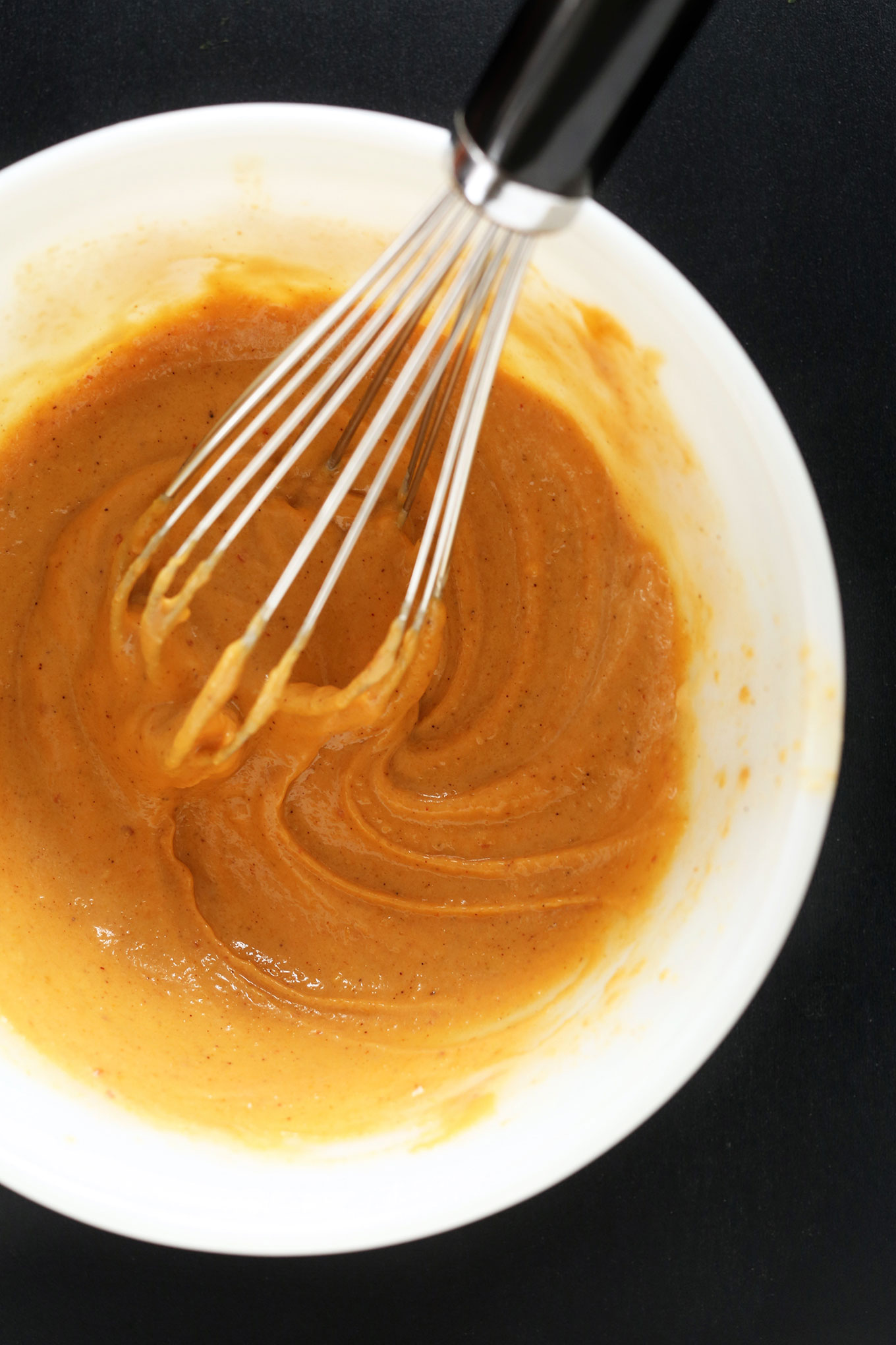 Using a whisk to add water to spreadable cheese to make Vegan Mexican Queso