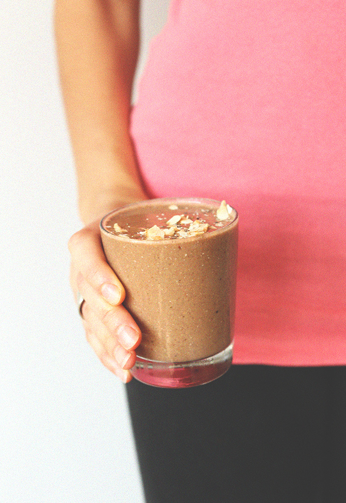 Holding a glass of Chocolate Coconut Chia Recovery Drink topped with toasted coconut