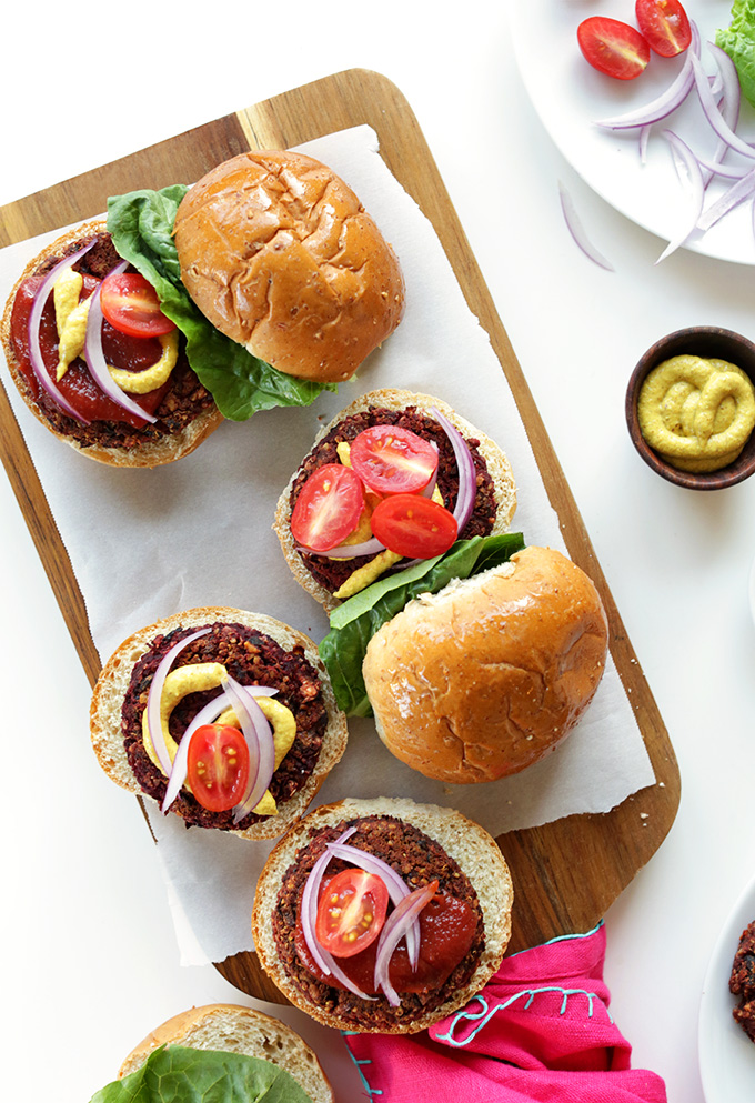 Cutting board with Vegan Black Bean Beet Burgers loaded with veggies and toppings