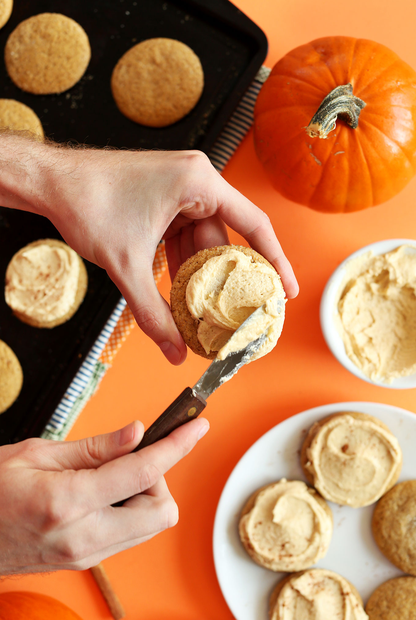 Using a butter knife to spread icing onto a Vegan Pumpkin Sugar Cookie