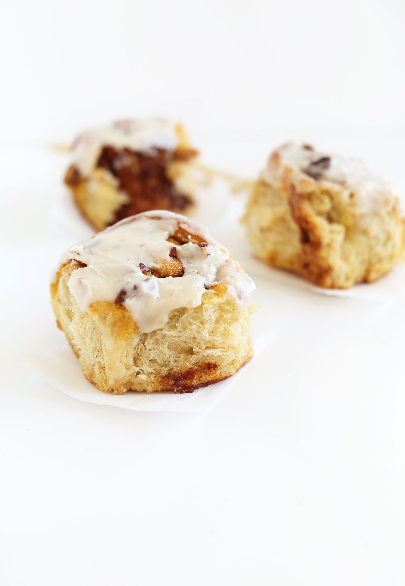 Freshly iced Pumpkin Cinnamon Rolls on squares of parchment paper