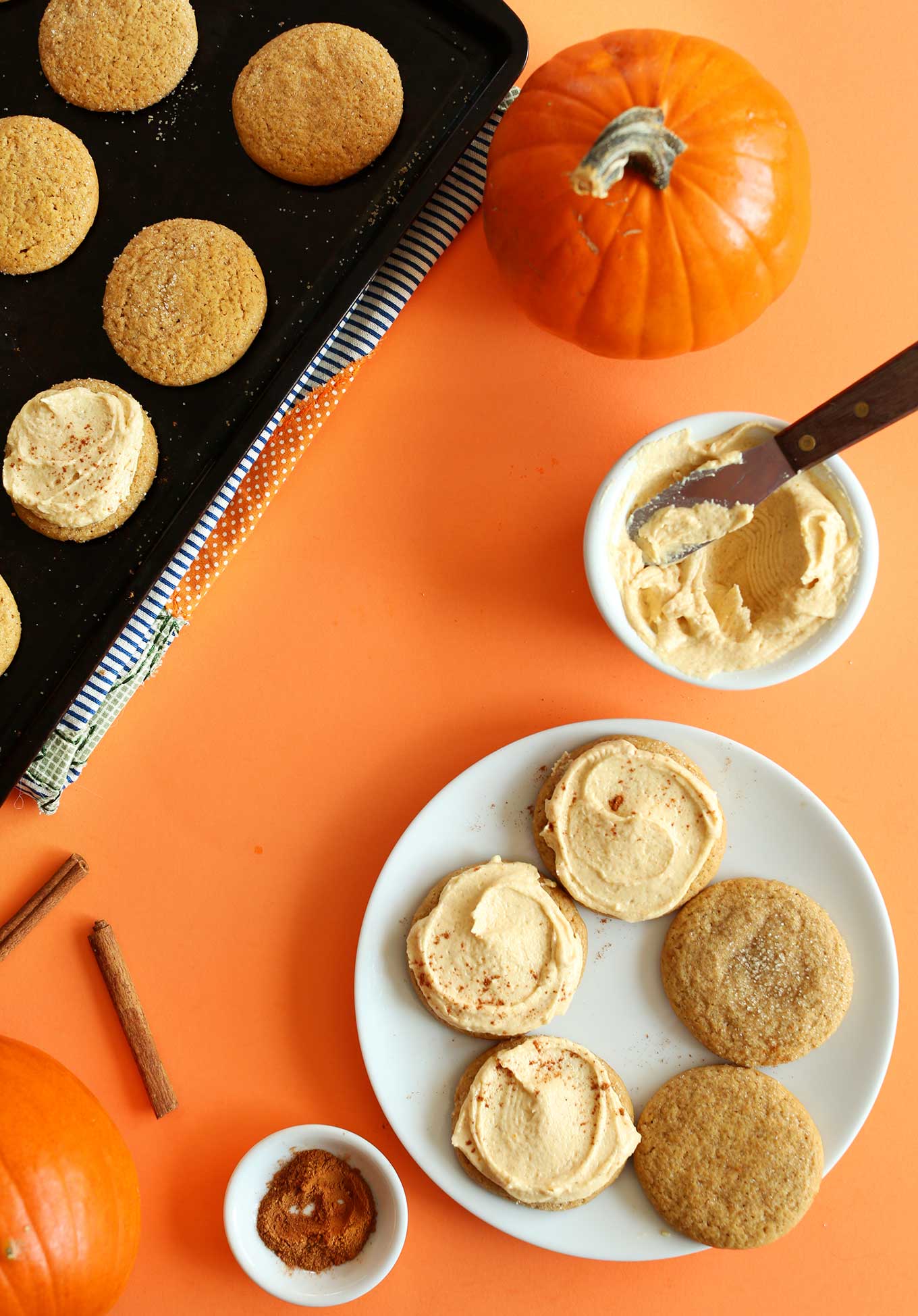 Plate and baking sheet with a partially-frosted batch of homemade Vegan Pumpkin Sugar Cookies