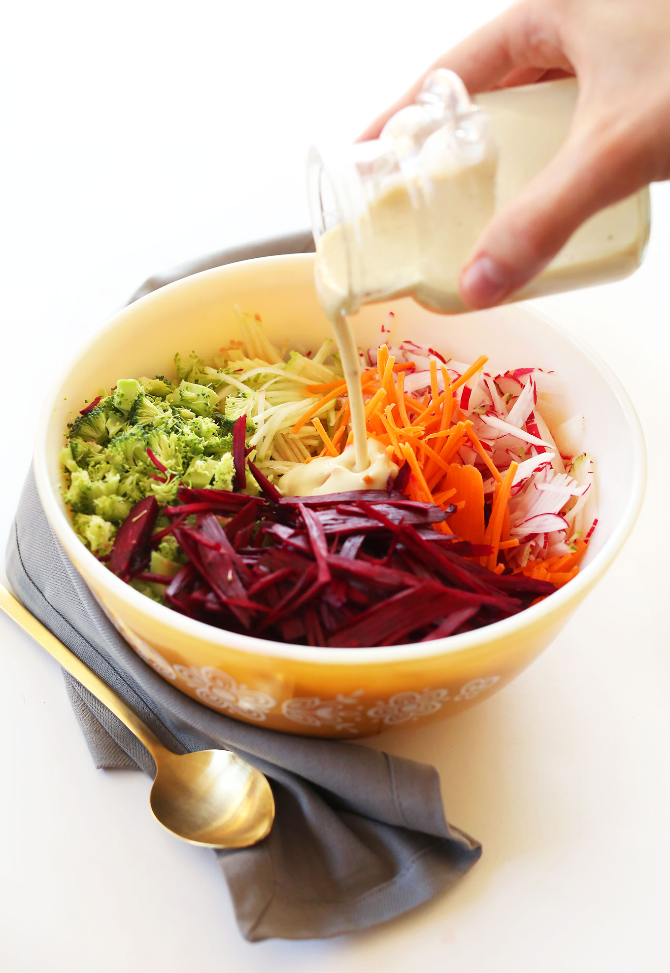 Pouring creamy vegan dressing onto our fall slaw