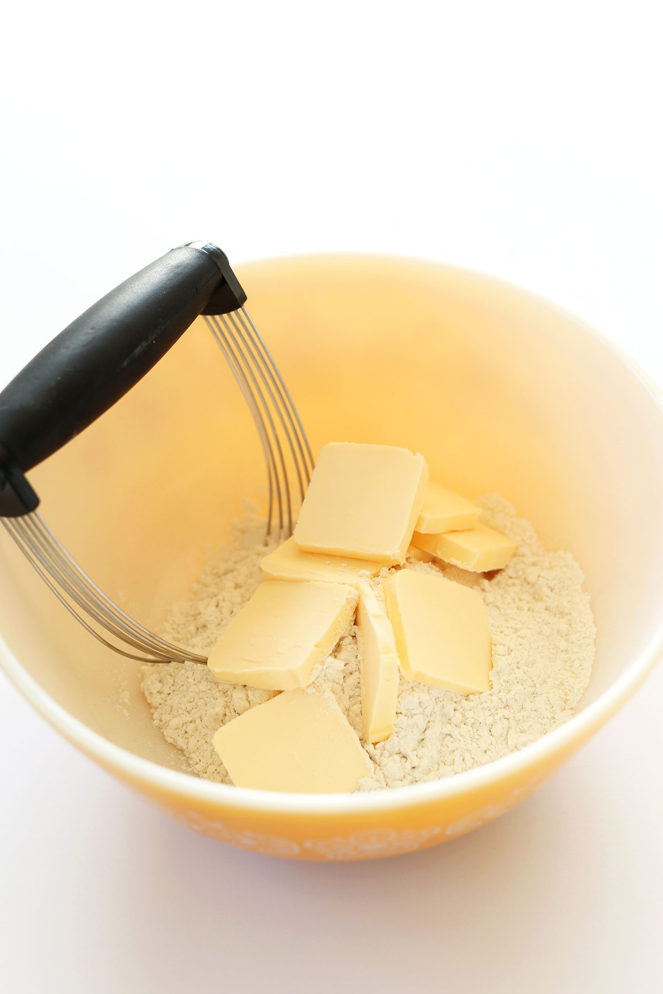 Pastry cutter to in a bowl with gluten-free flour and slices of vegan butter