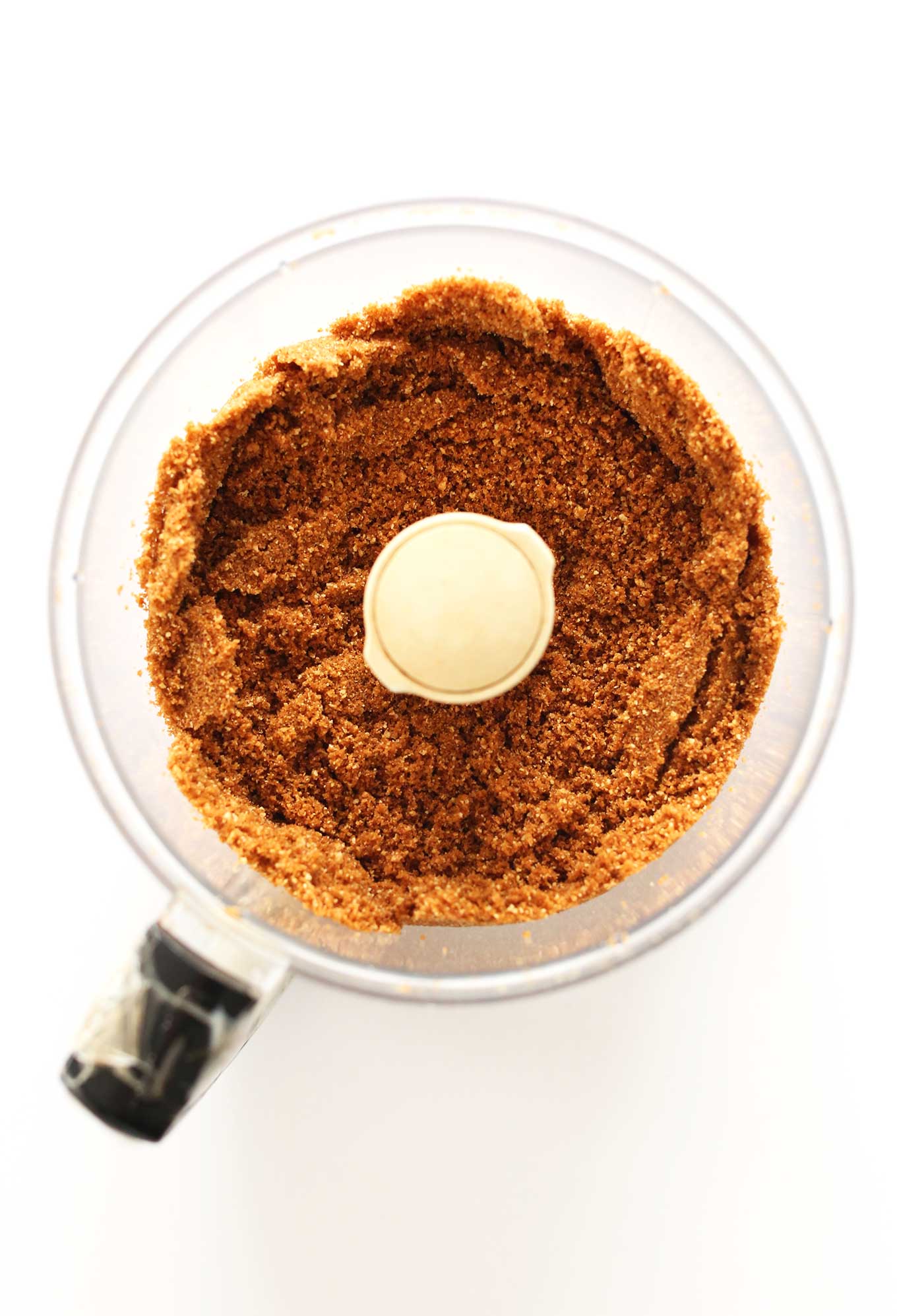 Food processor filled with crushed graham crackers for making cheesecake crust