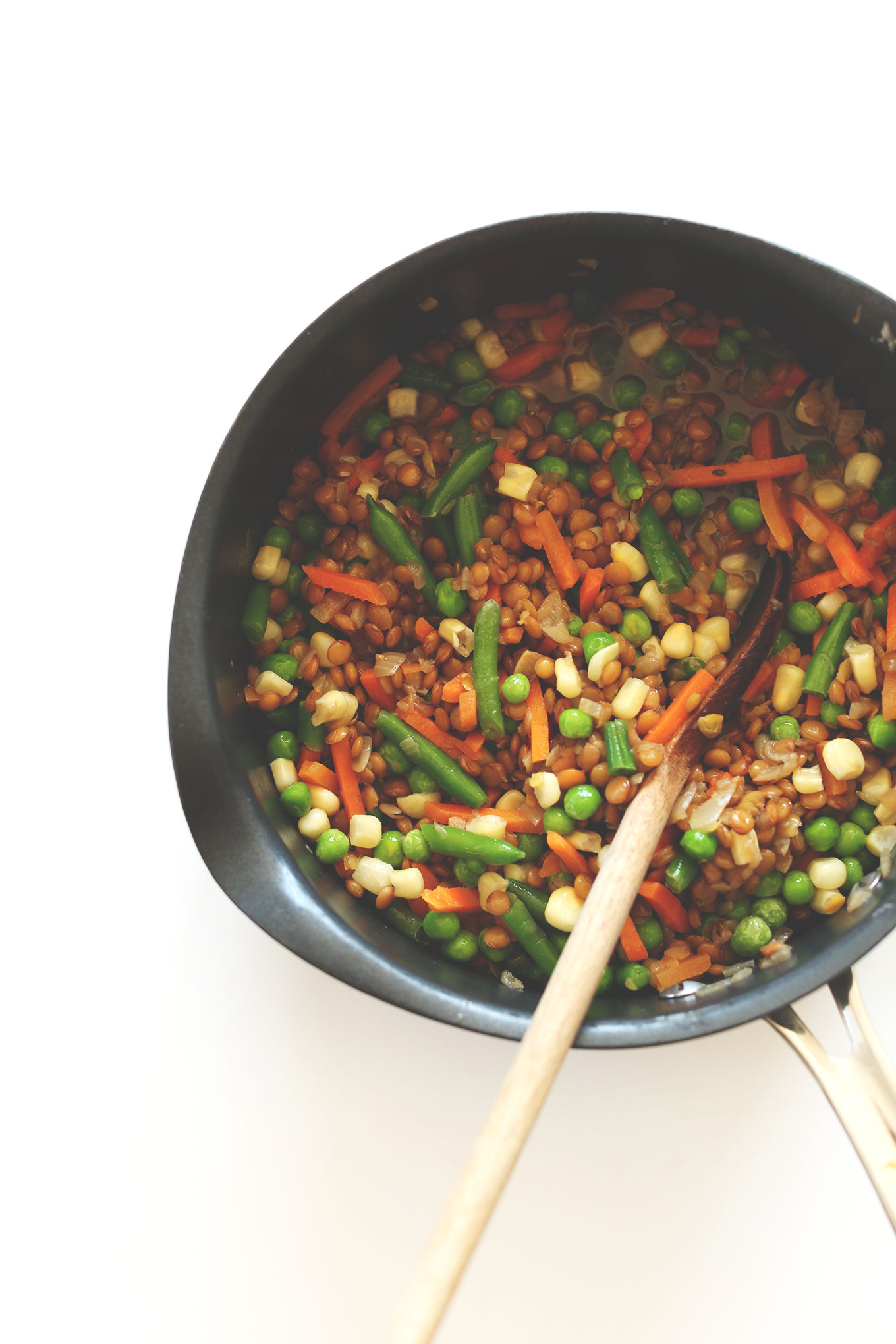 Using a wooden spoon to stir together lentils and vegetables for homemade Vegan Shepherd's Pie