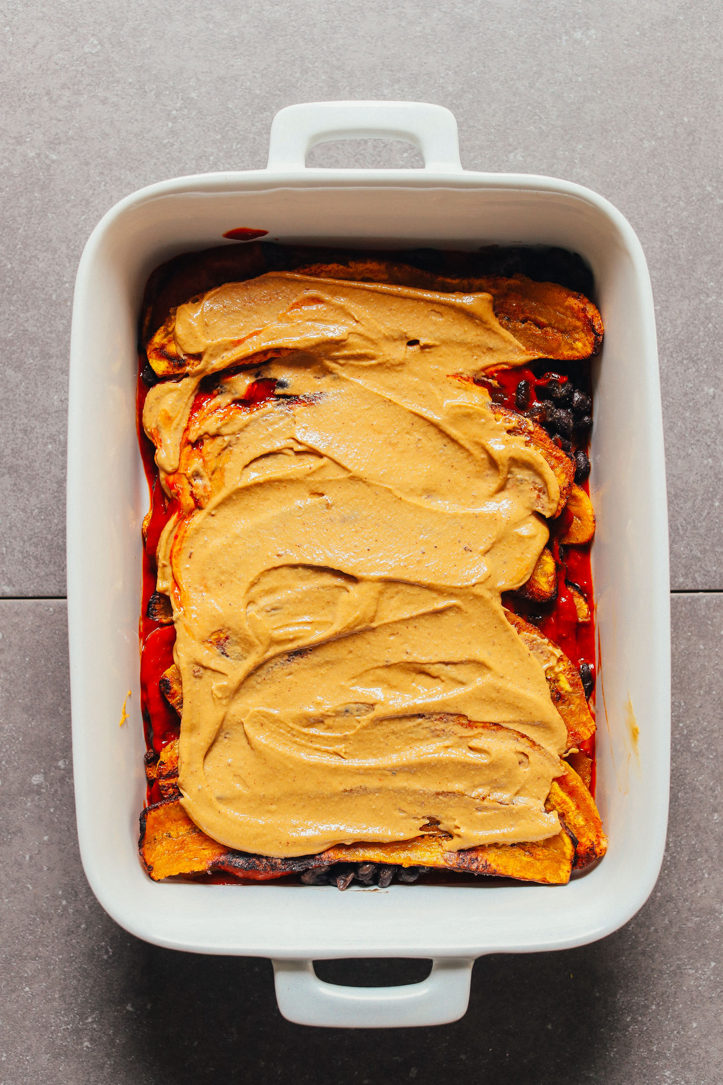 Showing a layer of Vegan Queso on our Plantain Black Bean Enchilada Bake
