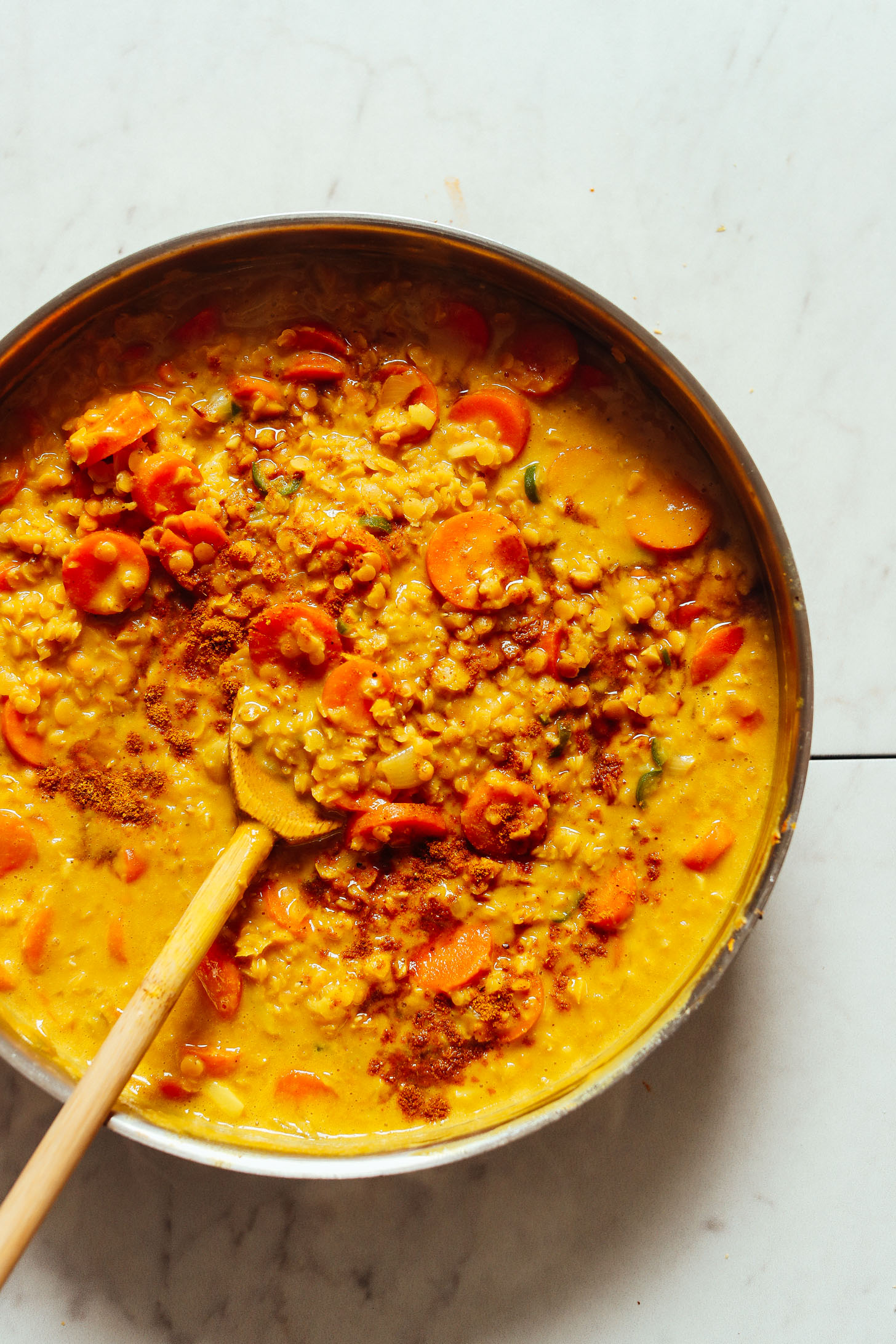 An overhead shot of golden curried lentil soup with carrots, coconut milk, and curry powder