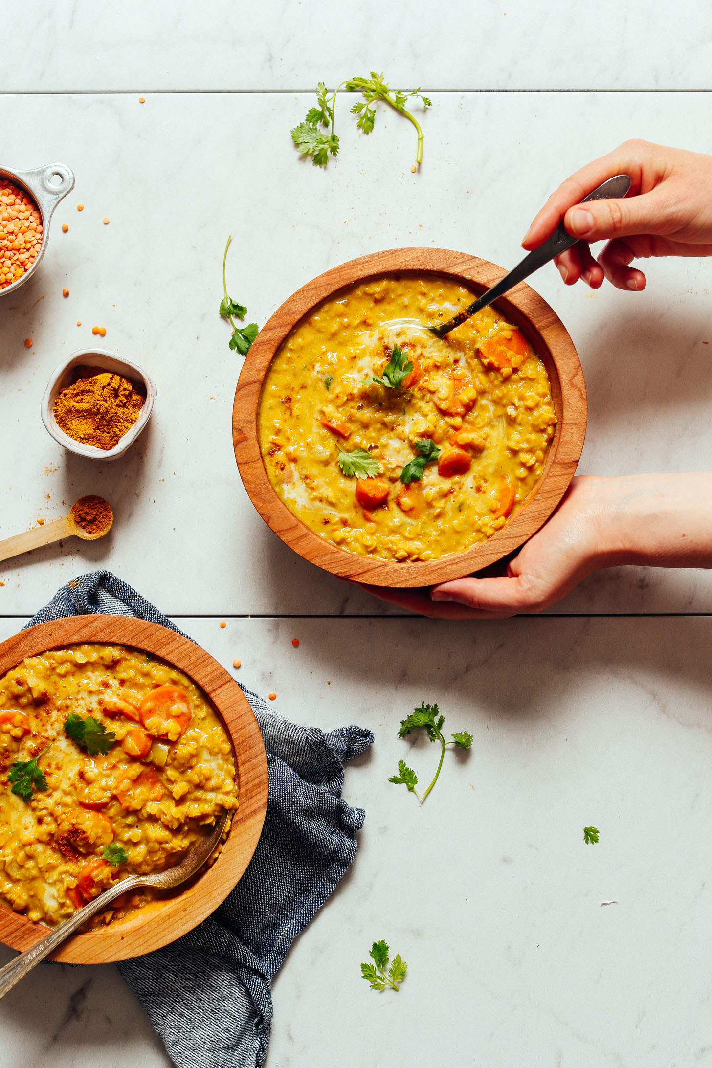 An overhead shot of two bowls of golden curried lentil soup with hands holding one bowl and taking a scoop
