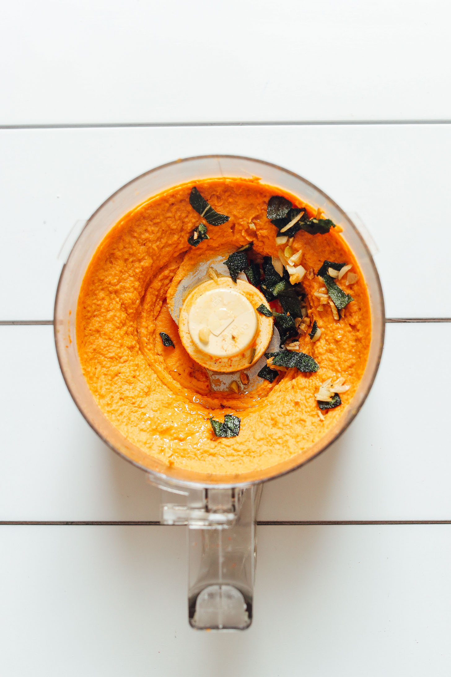 Food processor with freshly made White Bean Pumpkin Hummus topped with crispy sage pieces