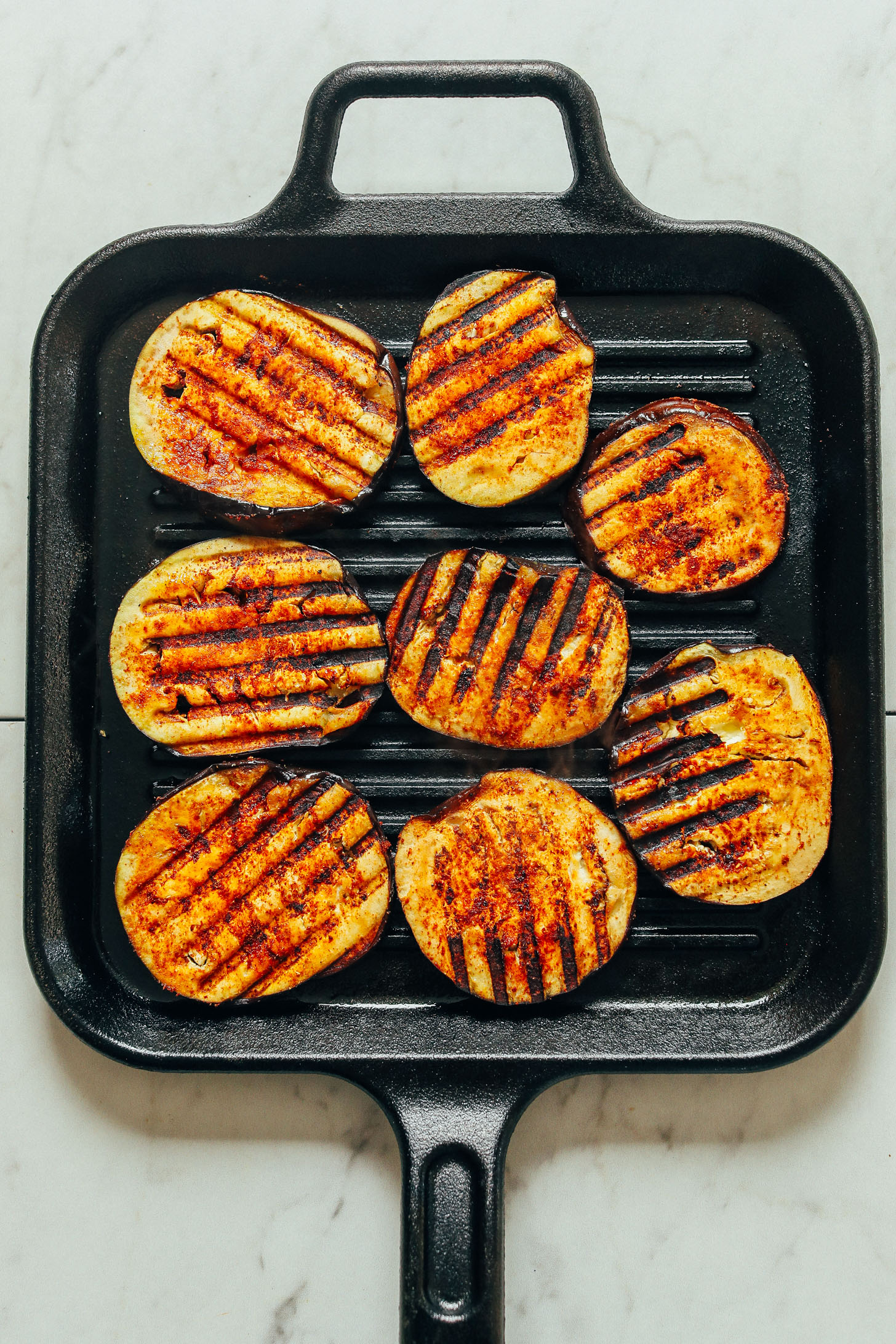 A overhead shot of eggplant slices seasoned with a spice blend and grill marks.