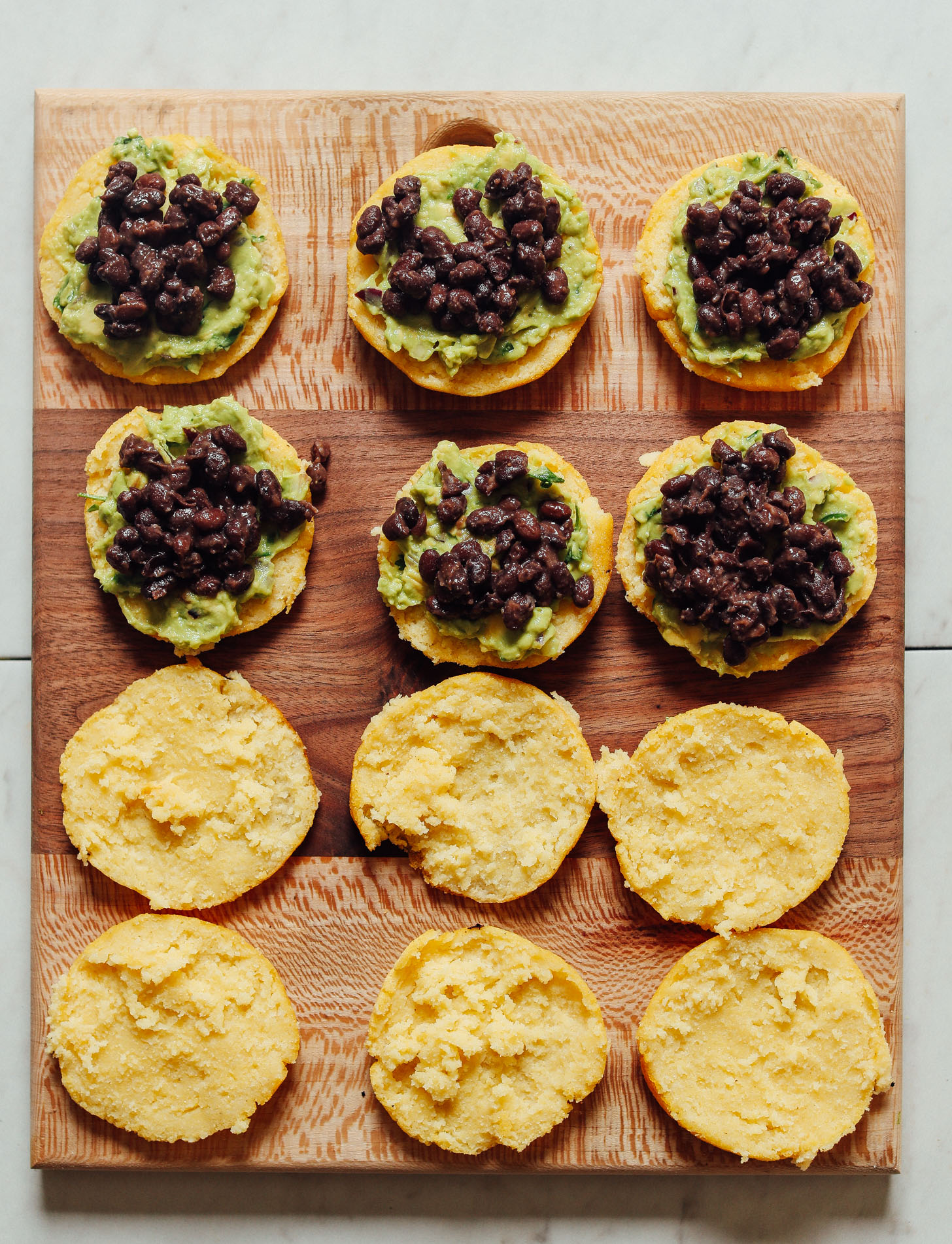 Wood cutting board with open-faced Arepa Sandwiches topped with guacamole and black beans
